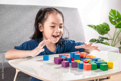 Asian girl plays with small wooden colorful toy blocks at home or kindergarten. A Girl enjoys playing with construction blocks for toddler kids. Education Development Construction creative toys Idea