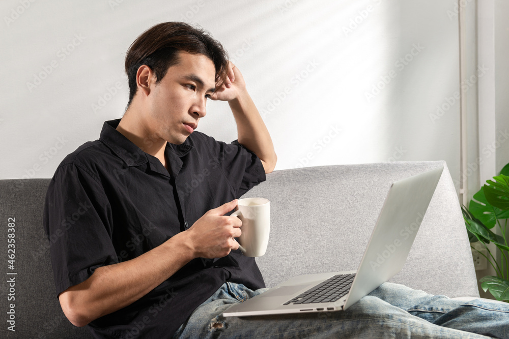 Bored Young man student or businessman video call via computer at home office with a cup of coffee in hand, using a laptop for video conference, sits on a couch, looking at a webcam talking online. Bored Young man student or businessman video call via computer at home office with a cup of coffee in hand, using a laptop for video conference, sits on a couch, looking at a webcam talking online.