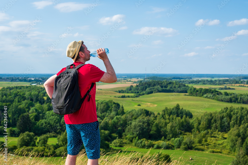 Traveler drinks water in the mountains.Hiker with backpack relaxing on top of the mountain in summer sunny day. Traveler drinks water in the mountains.Hiker with backpack relaxing on top of the mountain in summer sunny day.