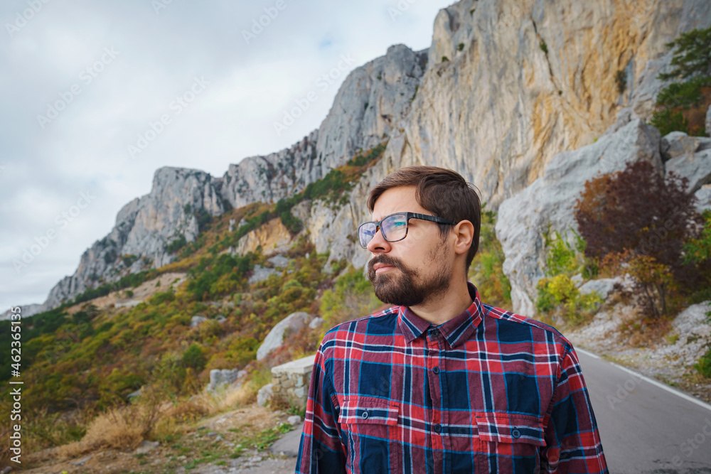Male hipster Traveler with backpack in plaid shirt and jeans hiking in the mountains travel, trekking in autumn countryside, road in the mountains