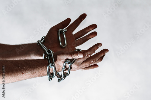 Men's hand in a steel chain.Steel chains in the hands of man on a gray wall background.Toned.Closeup,selective focus.Copy space.