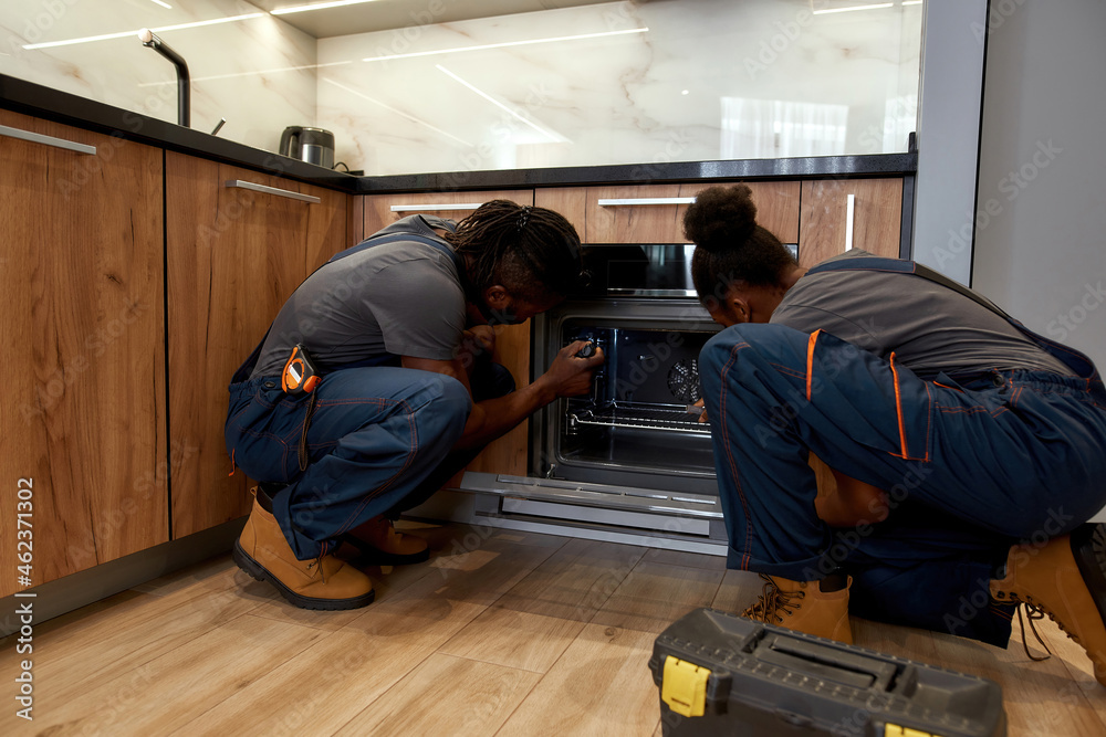 Man and woman workers repairing oven in kitchen Man and woman workers repairing oven in kitchen