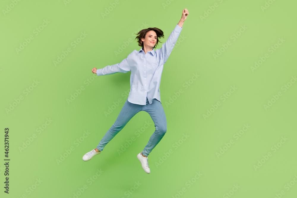Full body photo of happy cheerful cool woman jump up raise hand super hero empty space isolated on green color background Full body photo of happy cheerful cool woman jump up raise hand super hero empty space isolated on green color background