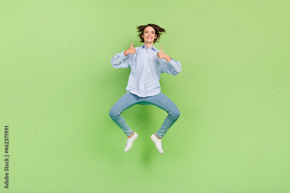 Full length photo of happy cheerful woman jump up make thumbs up advert isolated on green color background Full length photo of happy cheerful woman jump up make thumbs up advert isolated on green color background