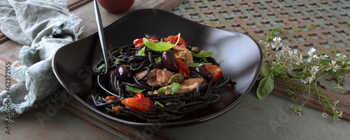 plate with black putanesca spaghetti on a wooden table photo