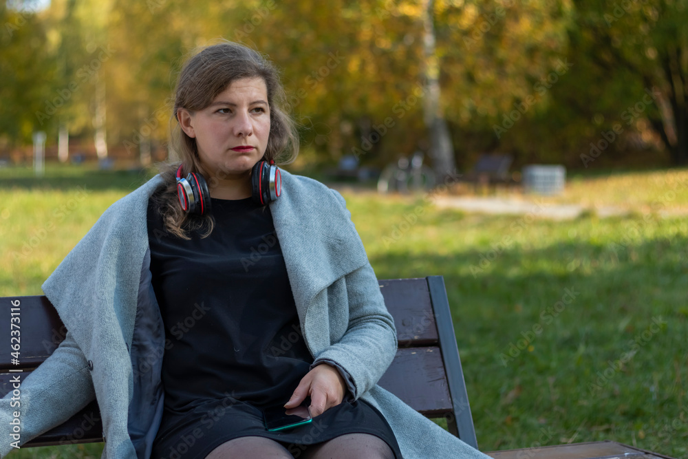 Portrait of a young beautiful Caucasian happy woman, about 35 years old with long hair and headphones in her ears. Cute girl walking in the park, close-up.