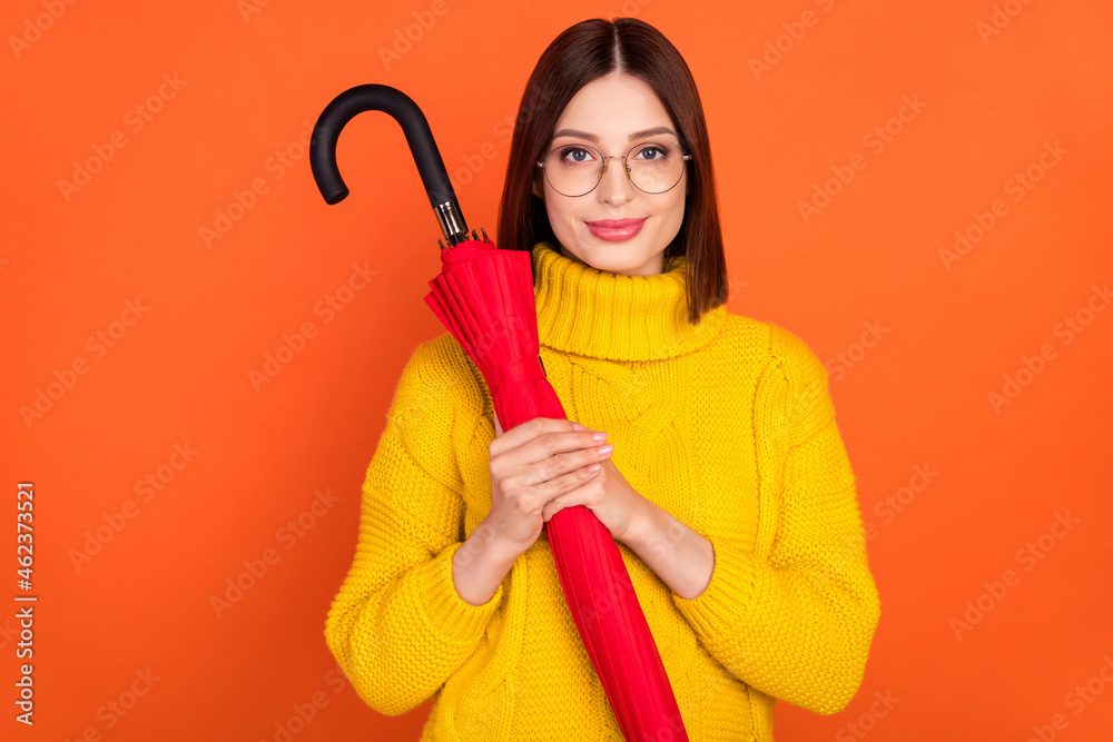 Photo of young woman happy positive smile hold umbrella weather wear glasses isolated over orange color background Photo of young woman happy positive smile hold umbrella weather wear glasses isolated over orange color background