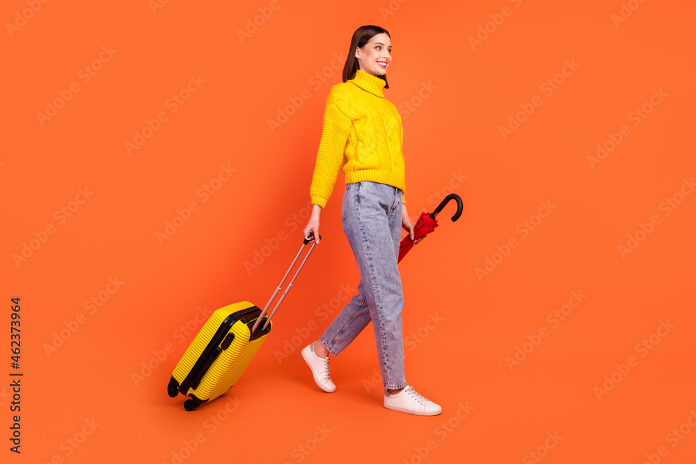 Full body profile side photo of young woman happy smile go walk tourist fly baggage trip isolated over orange color background Full body profile side photo of young woman happy smile go walk tourist fly baggage trip isolated over orange color background