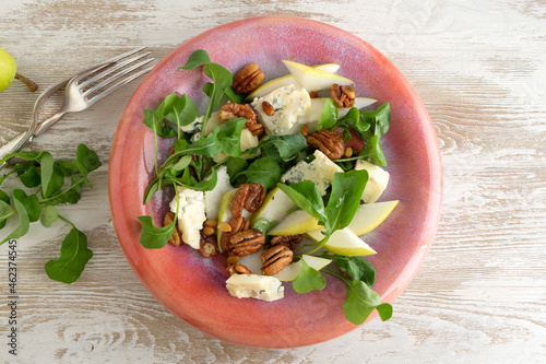 a plate of salad with arugula, pear, gorgonzola and nuts on a light table