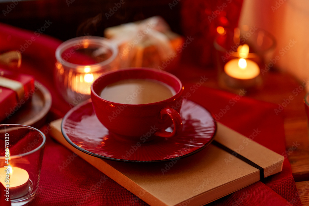 holidays, christmas and celebration concept - coffee in red ceramic cup with saucer and burning candles at home