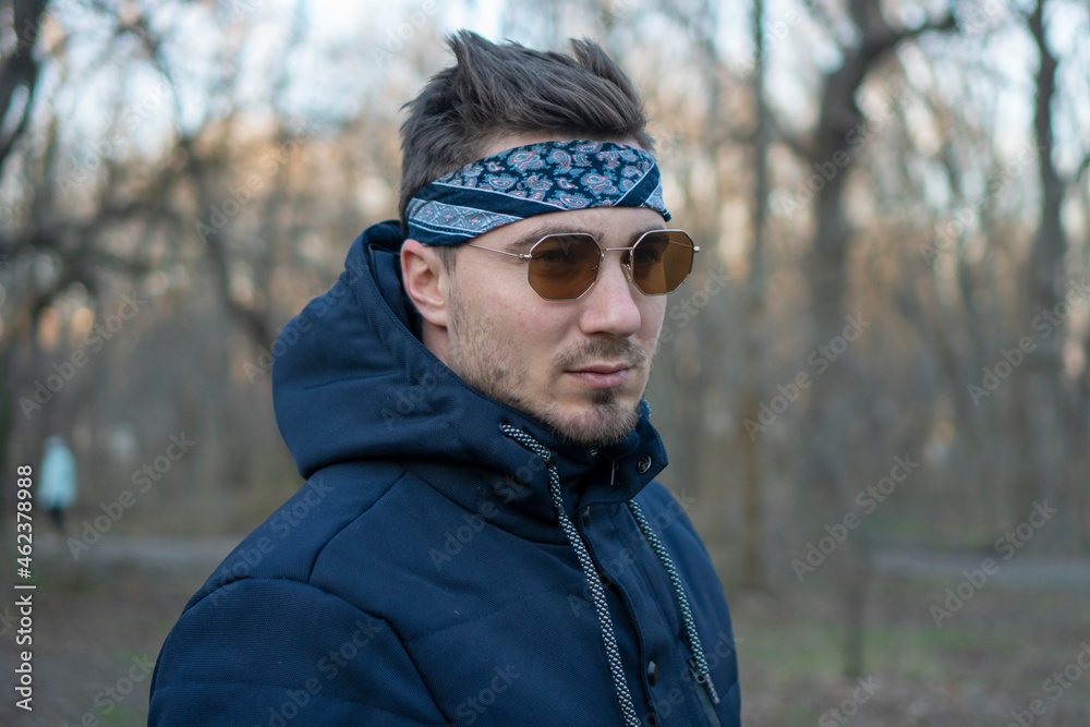 Portrait of a young and stylish man in sunglasses and a bandana. Male model showing fashion. Style concept. Portrait of a young and stylish man in sunglasses and a bandana. Male model showing fashion. Style concept.