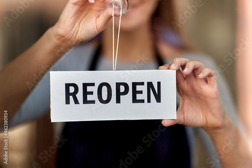 small business, reopening and service concept - happy smiling woman hanging reopen banner on window or door glass photo