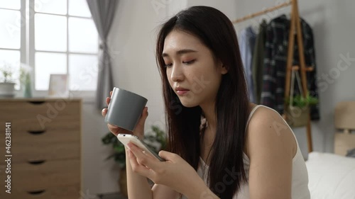 confused Korean woman staring at phone screen and checking the ridiculous posts on social media with a funny face while having coffee in the morning at home photo