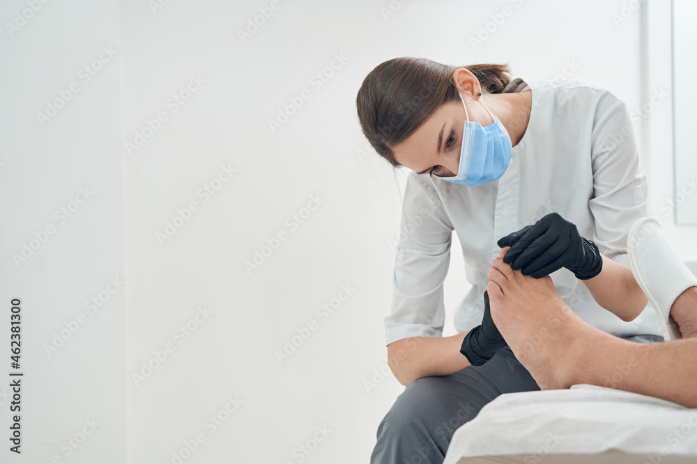 Woman cosmetologist examining male toes in cosmetology clinic Woman cosmetologist examining male toes in cosmetology clinic