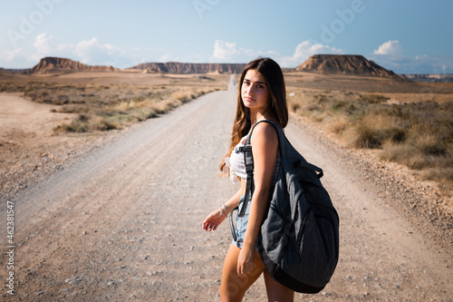 Young caucasian woman with a grey backpack walking in the middle of a dessert at Bardenas  Navarre  Basque Country.