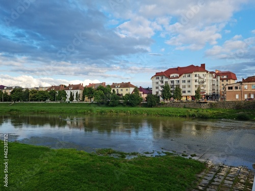 Natural beauty of blue sky and calm water of river in Mukachevo, Ukraine. Beautiful landscape with river and houses at sunset. Scenic view of the old town embankment on a cloudy summer day at dusk. © Liudmyla Leshchynets