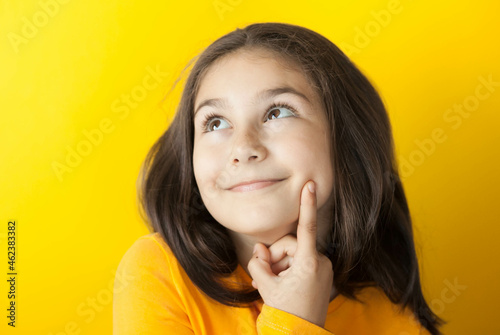 Portrait of a cute thoughtful child girl on yellow background in yellow t-short. People dream. Space for text.