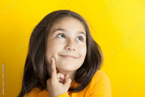 Portrait of a cute thoughtful child girl on yellow background in yellow t-short. People dream. Space for text. © kaganskaya115