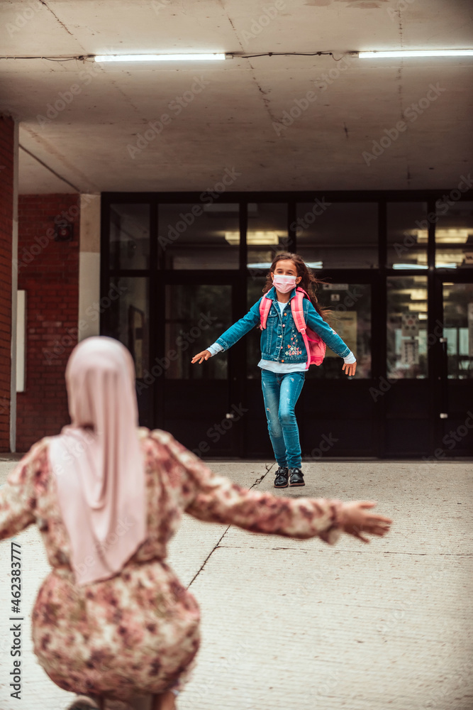 Fototapeta premium Schoolgirl runs into her mothers arms after school.New normal. Education during the Covid-19 pandemic. Selective focus.