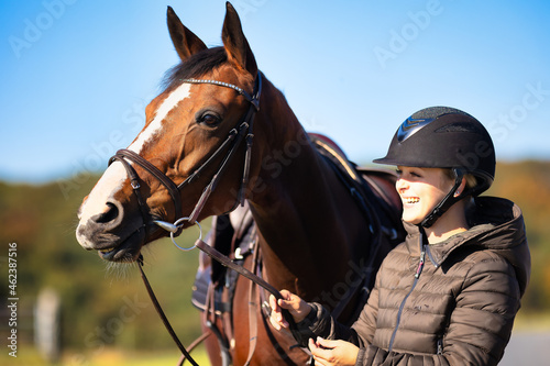 Horse saddled in head portrait from the front, horse looks attentively to the right with raised upper lip and the rider laughs and holds it by the reins..