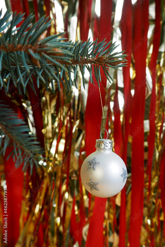 a glass white round toy hangs on a branch of a Christmas tree on a golden background of garlands. decorations for the Christmas tree