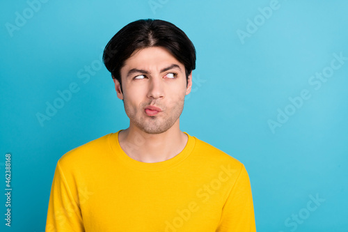 Photo of millennial unsure guy look empty space wear yellow shirt isolated on blue color background