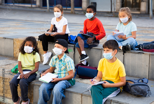 Portrait of focused diligent schoolchildren in face masks during lesson outside school in warm autumn day. New lifestyle in coronavirus pandemic