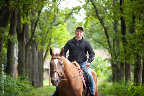 Man riding a horse in a beautiful forest, smiling, looking at the camera © Mariana