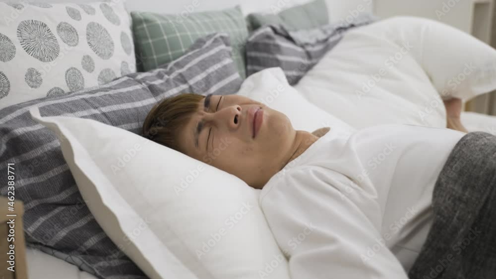 closeup of a sleepless asian male covering his head and ears with pillow while suffering neighbor noise in the early morning on bed at home. closeup of a sleepless asian male covering his head and ears with pillow while suffering neighbor noise in the early morning on bed at home.