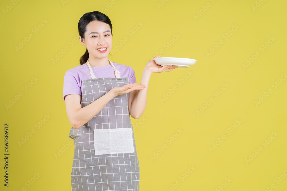 Young Asian housewife posing on yellow background Young Asian housewife posing on yellow background