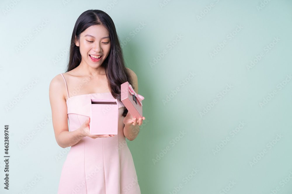 Beautiful young Asian woman holding pink gift box on green background Beautiful young Asian woman holding pink gift box on green background