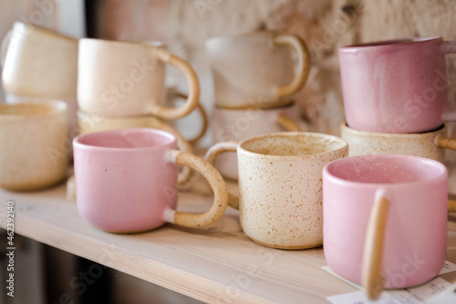 Handmade empty pink and yellow clay mugs composition on a wooden shelf with bricks in the background.