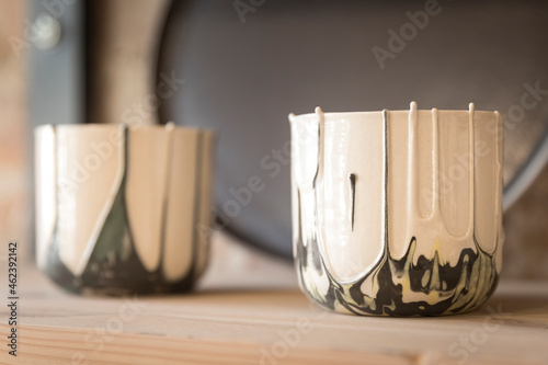 Handmade empty clay mugs composition, painted with warm white and green, on a wooden shelf in a shop