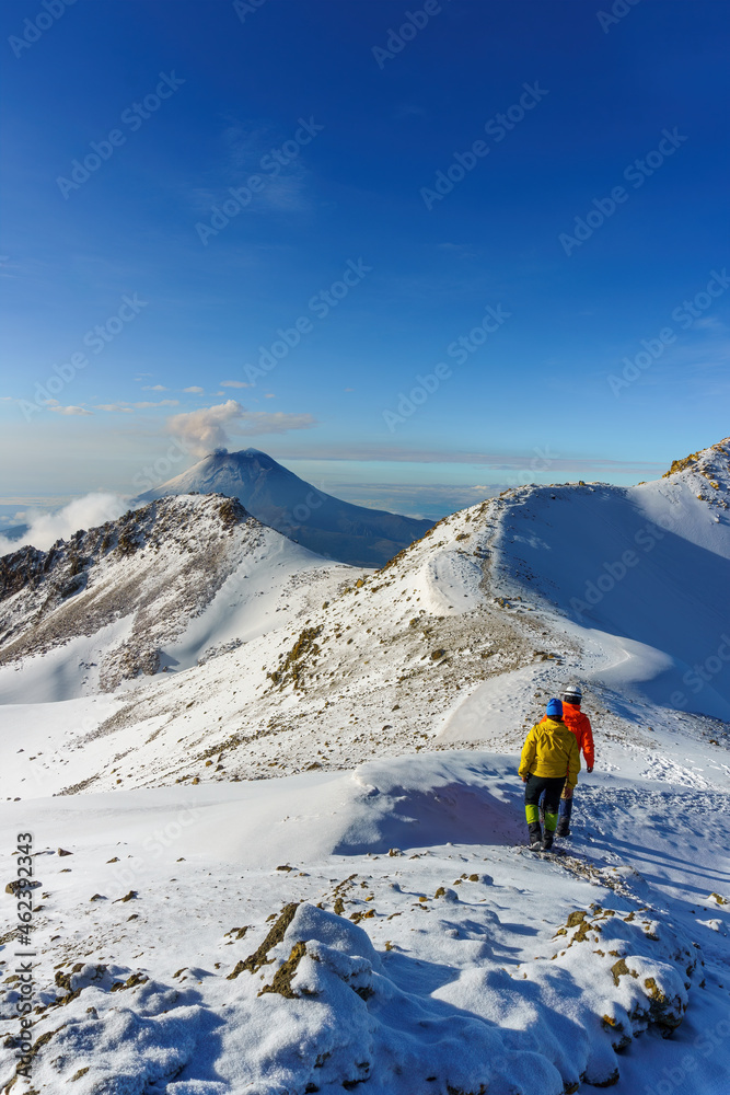 hikers walking on snow, on top of a snowy volcanic mountain