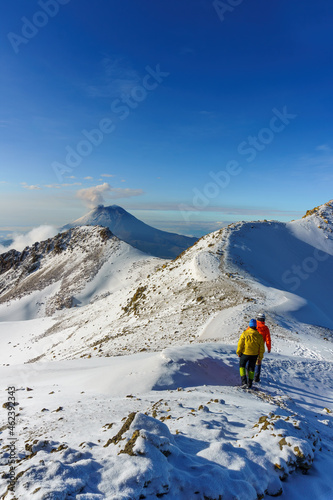 hikers walking on snow, on top of a snowy volcanic mountain