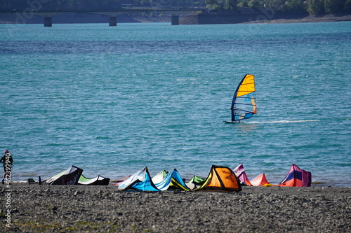windsurfing on the lake and colorful kite surfing sails on the beach in serre ponçon alps france
