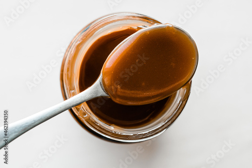 Homemade salted caramel in glass jar, white background, spoon with caramel