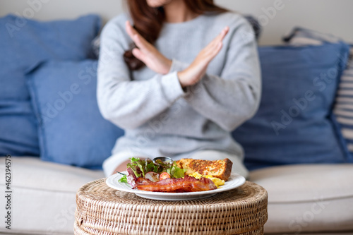 A woman making crossed arms hand sign to refuse food on the table for dieting and healthy eating concept