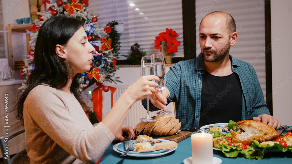 Man and woman clinking glasses of champagne at festive dinner, celebrating christmas eve with chicken and alcohol. Couple enjoying meal for traditional holiday celebration. People eating Man and woman clinking glasses of champagne at festive dinner, celebrating christmas eve with chicken and alcohol. Couple enjoying meal for traditional holiday celebration. People eating