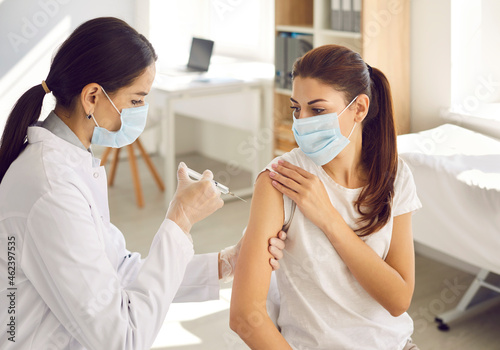 Female nurse in gloves giving a flu shot to a patient during a seasonal vaccination campaign. Beautiful young woman wearing a mouth covering getting a Covid-19 vaccine at a modern medical center