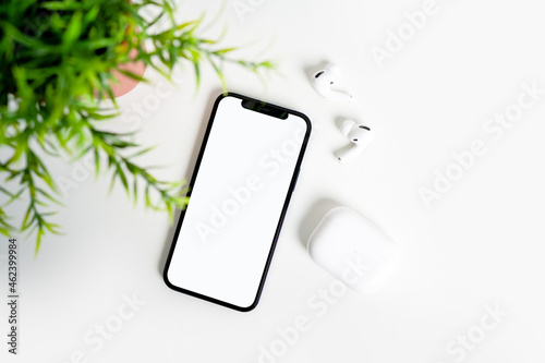 On the white table there is a smartphone with a white display and Bluetooth headphones.