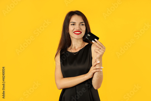 Girl in black dress with credit card on yellow background