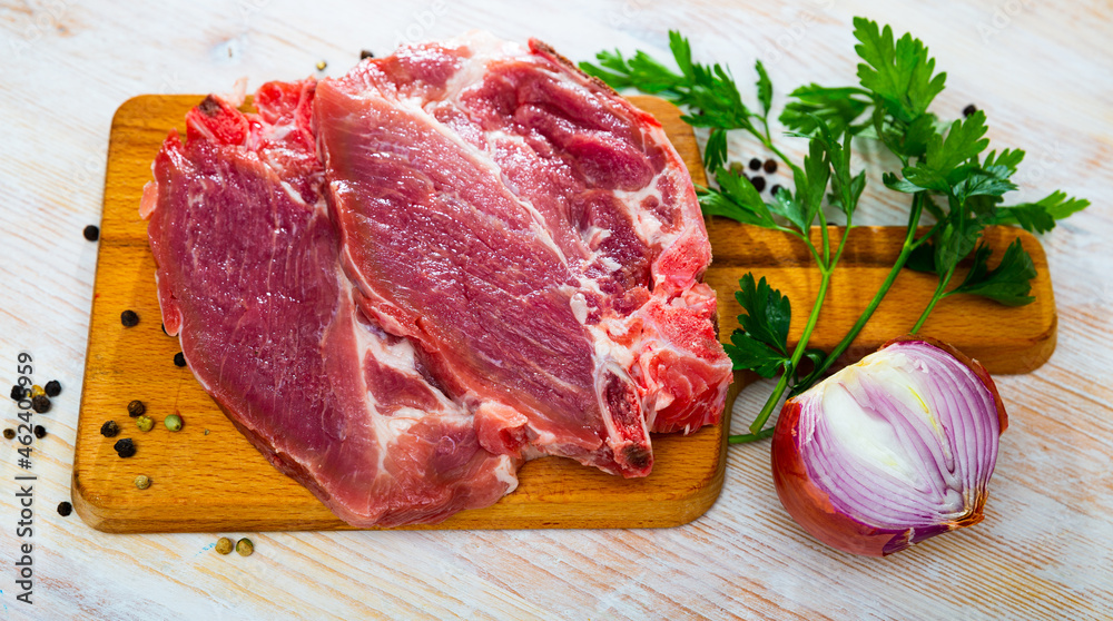 Fototapeta premium Raw pork chops served on wooden board with purple onion, parsley and black pepper