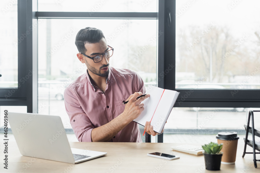 Arabian businessman pointing at notebook during video chat on laptop in office Arabian businessman pointing at notebook during video chat on laptop in office