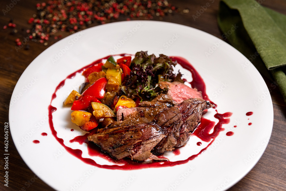Chateaubriand of tender beef in Bordeaux wine sauce with vegetable sauté. Large plate of food on a dark brown wooden backdrop. Chateaubriand of tender beef in Bordeaux wine sauce with vegetable sauté. Large plate of food on a dark brown wooden backdrop.
