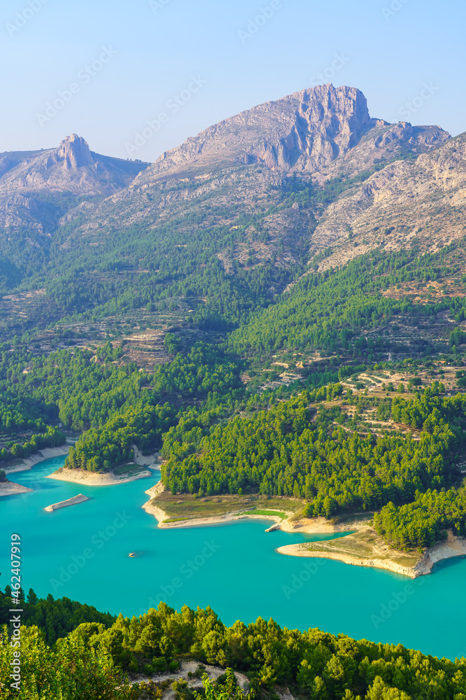 Blue lake in the green valley next to high rocky mountains. Guadalest Alicante.