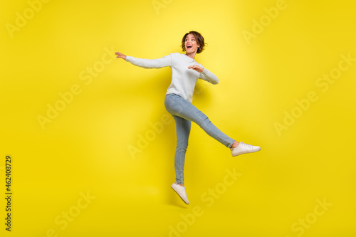 Full size photo of impressed young brunette lady jump wear pullover jeans sneakers isolated on yellow background