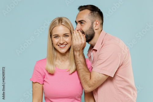 Young couple two friends family man smiling fun woman wear casual clothes whisper gossip tell secret behind her hand sharing news together isolated on pastel plain light blue color background studio