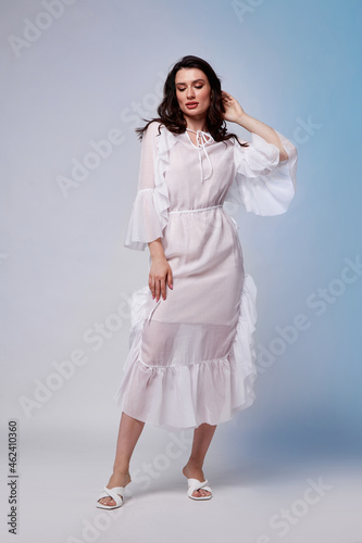 Beautiful woman fashion model makeup brunette hair perfect body shape tanned skin wear clothes summer collection organic long white silk dress stylish sandals shoes, accessory jewelry earrings date. © indiraswork