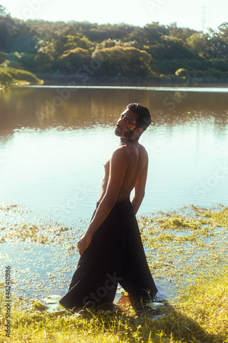Canvas Print portrait of a dark skinned Indian man by a lake, shirtless, with make up, surrou